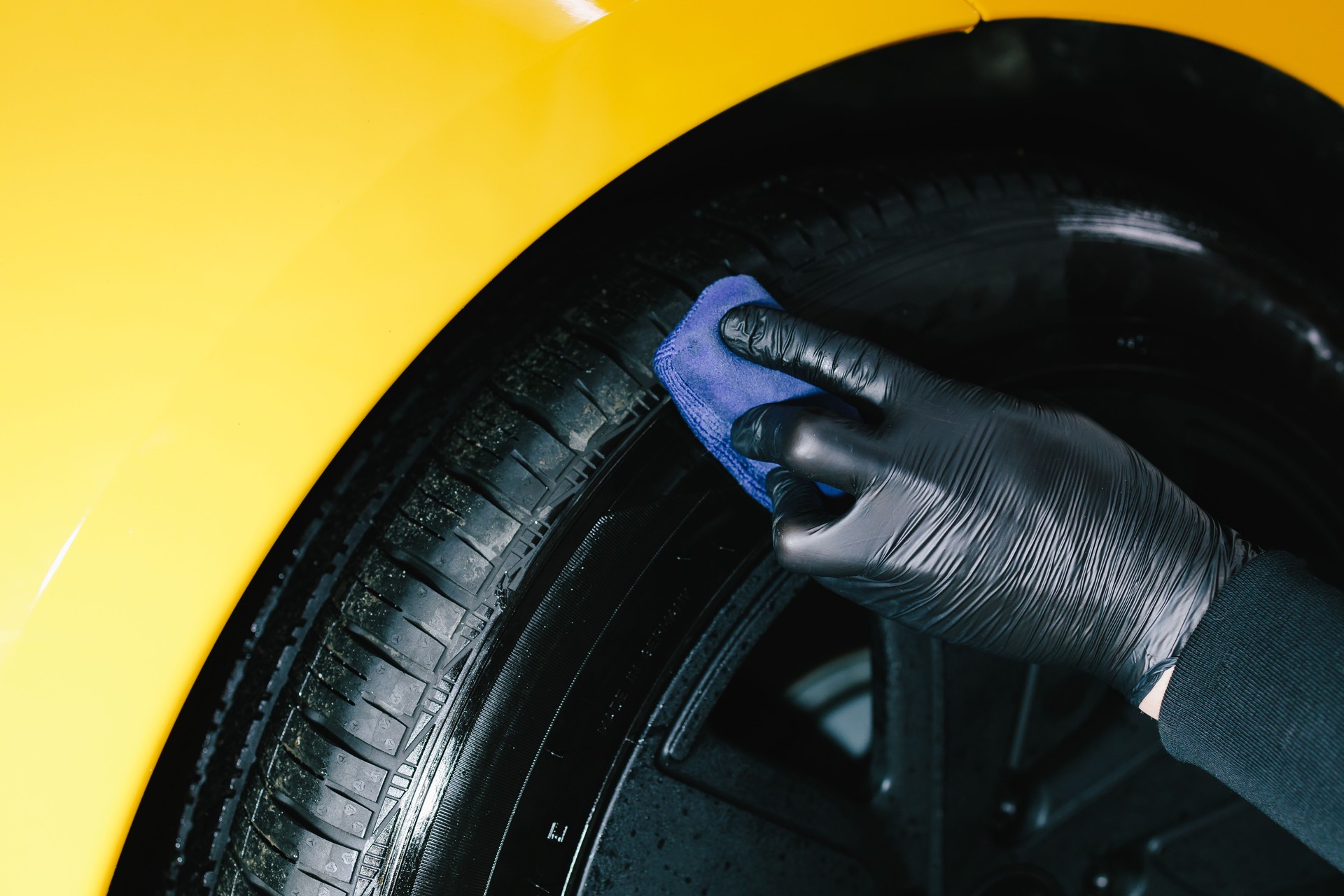 Blackening of tire wheel of car using sponge with chemical blackening of rubber in detailing auto service. Mechanic applies a product to a black tire using a blue applicator.